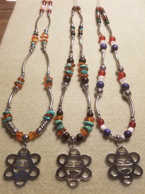 Three beaded necklaces with curved silver tube beads and matching silver petroglyph-style face pendants.
