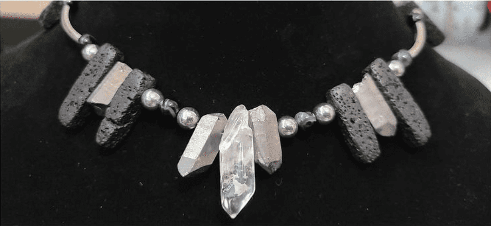 Close-up of a necklace strung with black lava stone bars and raw clear quartz points, on a black display bust.