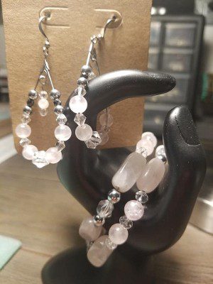 Rose quartz and silver earrings displayed with a matching bracelet on a black hand-shaped jewelry stand.