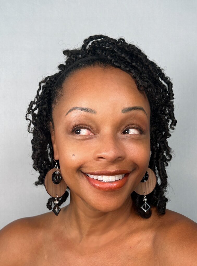 The model smiling, wearing round wooden disc earrings with a smoky glass bead and a dark diamond-shaped drop.