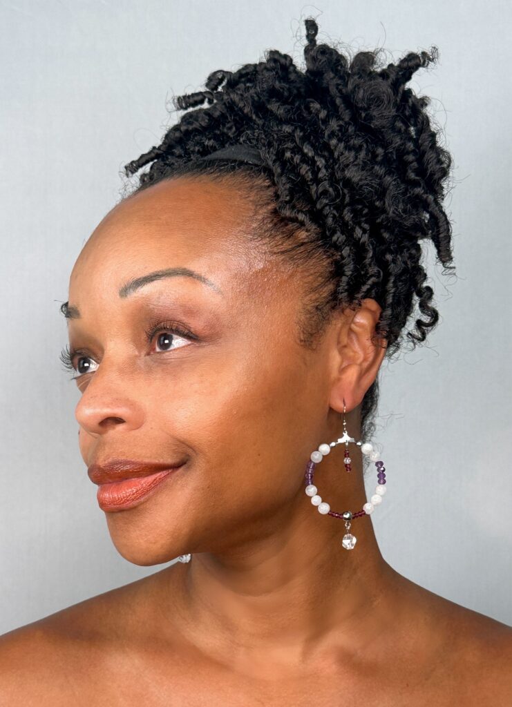 Side profile of the model wearing a large hoop earring strung with white pearl and deep purple beads and a faceted crystal drop.
