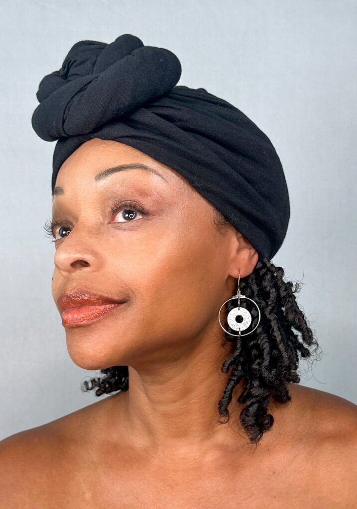 The model in a black head wrap wearing a silver open-circle earring with a textured disc suspended at its centre.