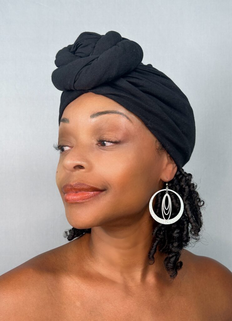 The model in a black head wrap wearing a large silver hoop earring with a textured outer ring and a leaf-shaped inner form.