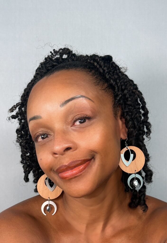 The model wearing large round wooden earrings layered with pale grey chevron and crescent shapes and a small faceted bead.
