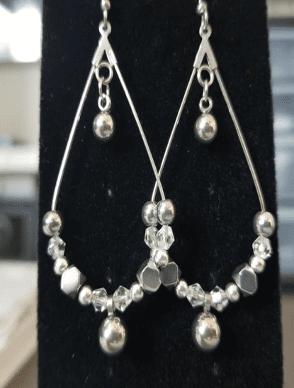 Silver teardrop chandelier earrings strung with clear crystal and silver beads, on a black display stand.
