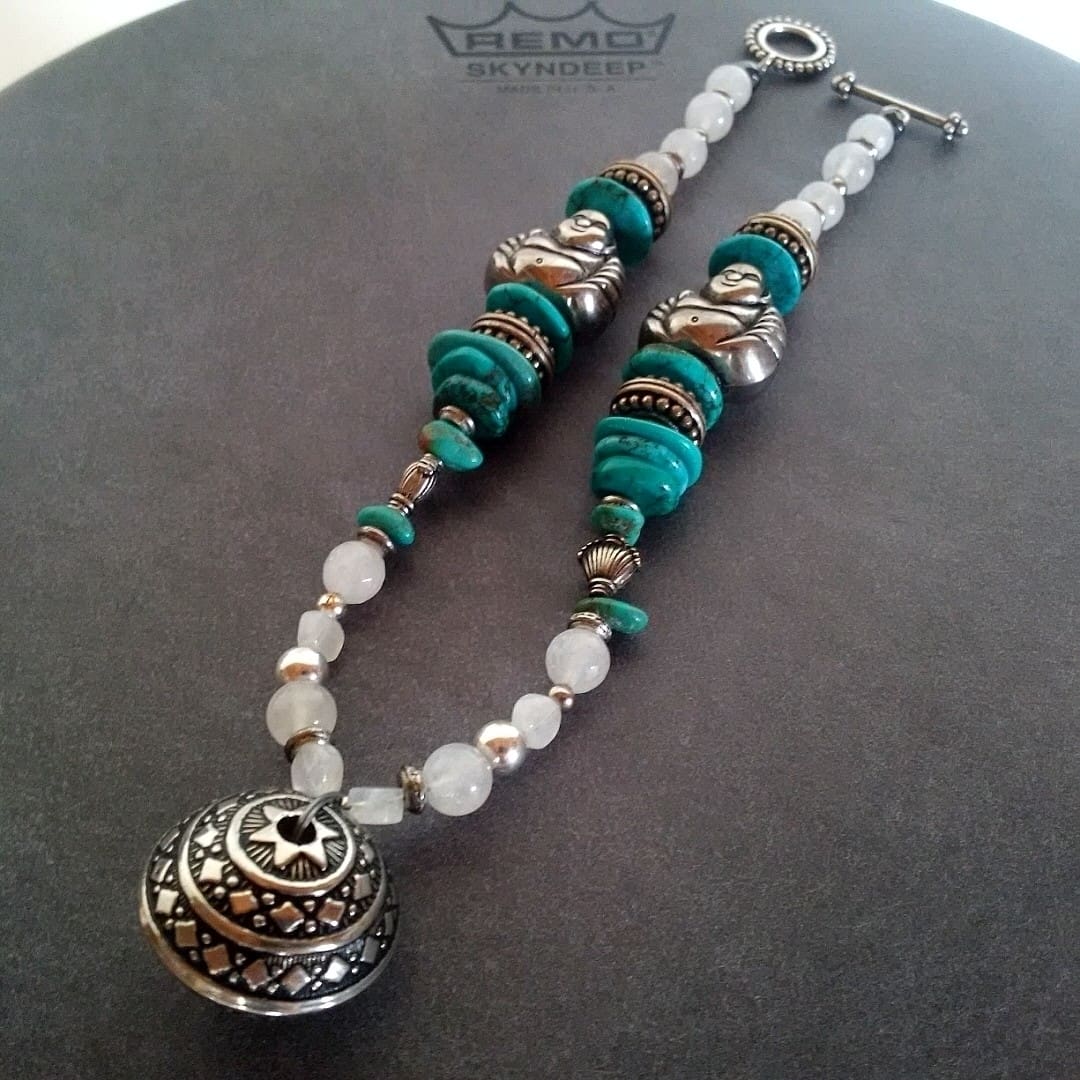 A necklace of turquoise, white quartz and silver beads with seated figure beads and a domed embossed silver pendant, resting on a drum head.