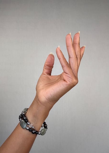 A raised hand against a grey backdrop wearing a double-wrapped bracelet of grey labradorite and black beads with silver accents.