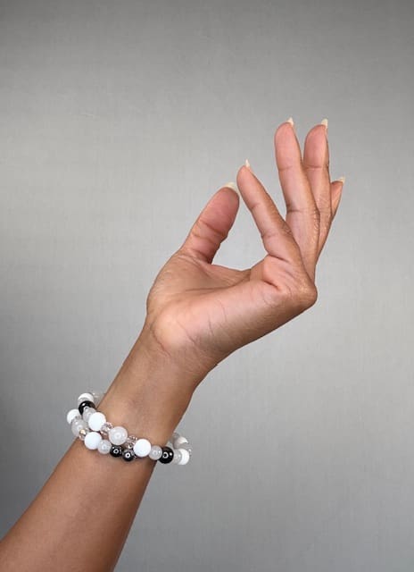 A raised hand against a grey backdrop wearing a double-wrapped bracelet of white and clear beads with black and silver accents.