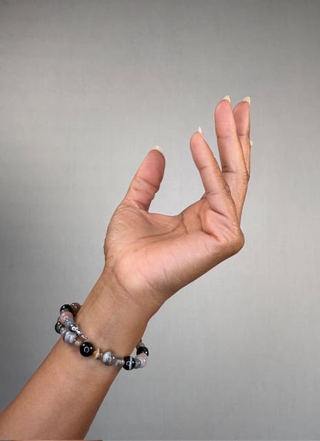 A raised hand against a grey backdrop wearing a double-wrapped bracelet of black onyx and grey agate beads.